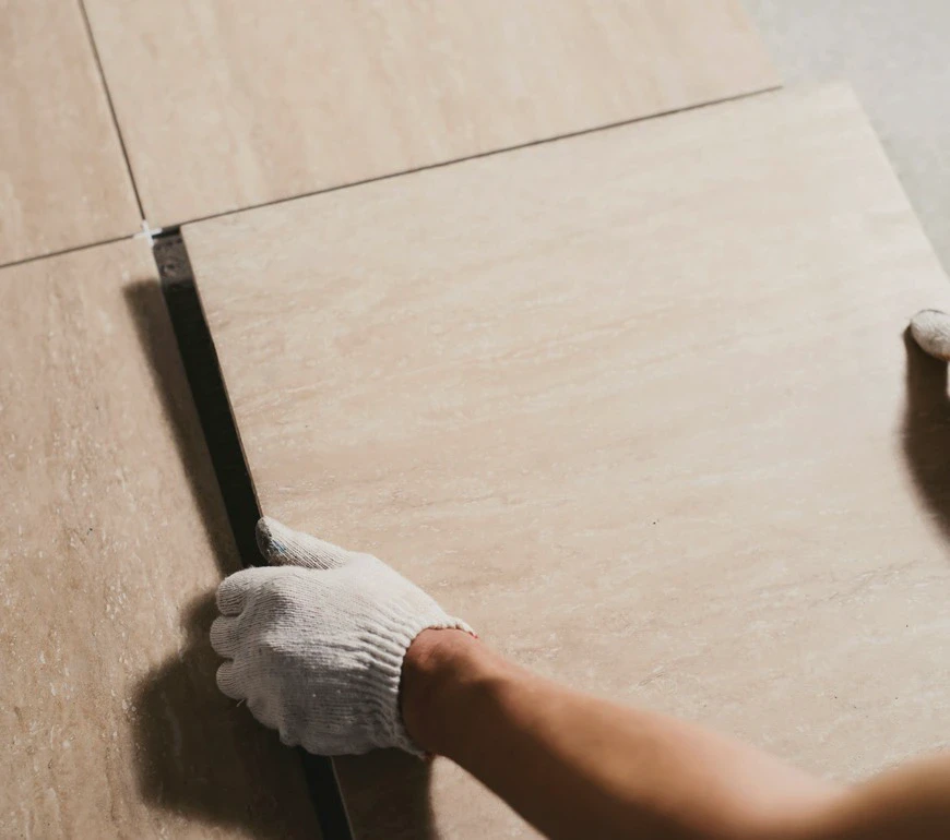 Ręka w roboczej rękawicy ustawiająca ceramiczną płytkę podczas prac glazurniczych.