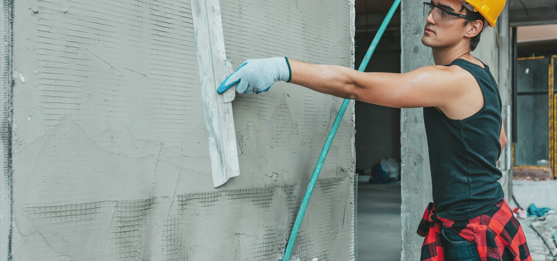 Osoba nakładająca zaprawę lub tynk na ścianę za pomocą pacy w trakcie prac budowlanych